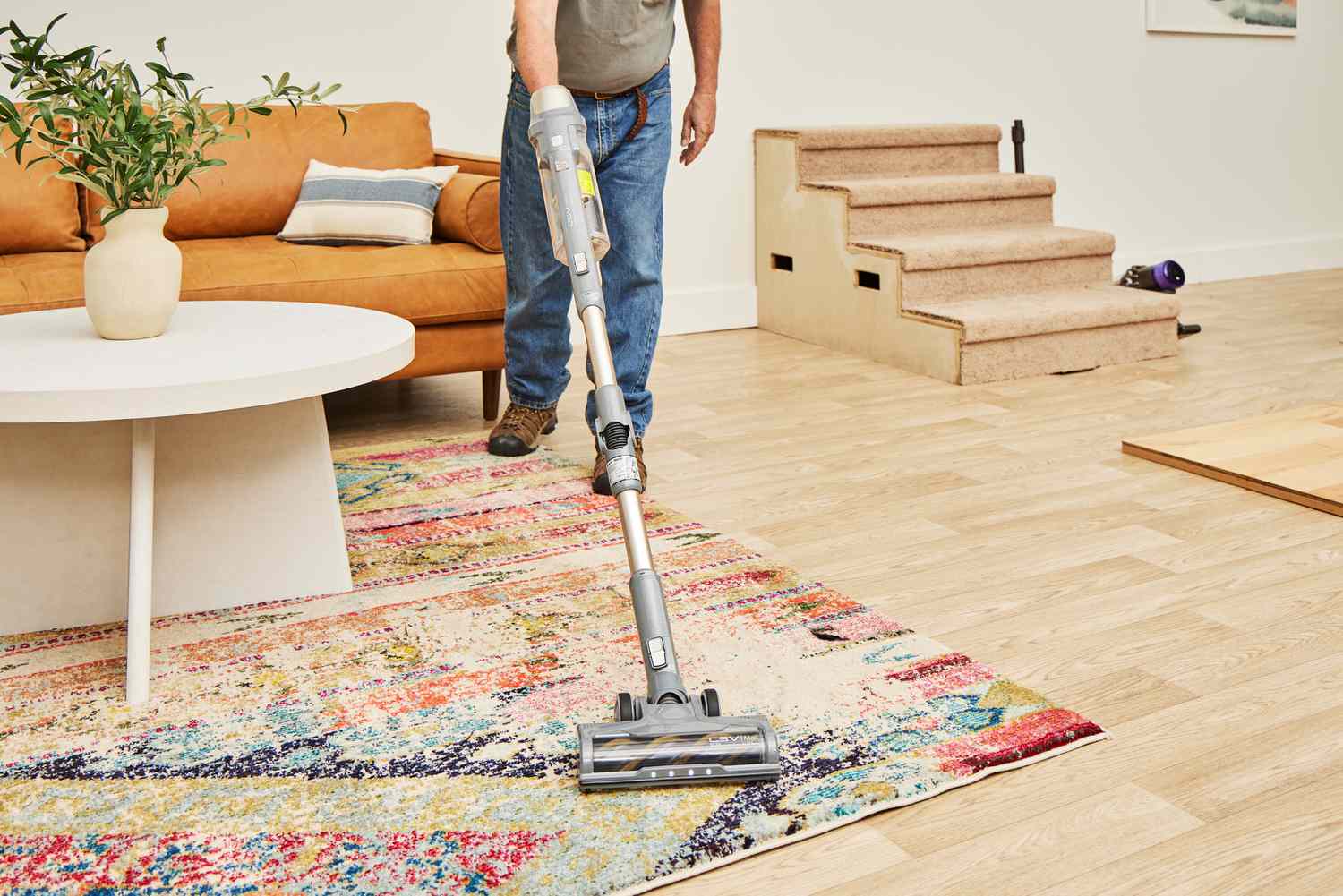 A person vacuuming a rug in a living room setting with the Kenmore DS4095 Brushless Cordless Stick Vacuum