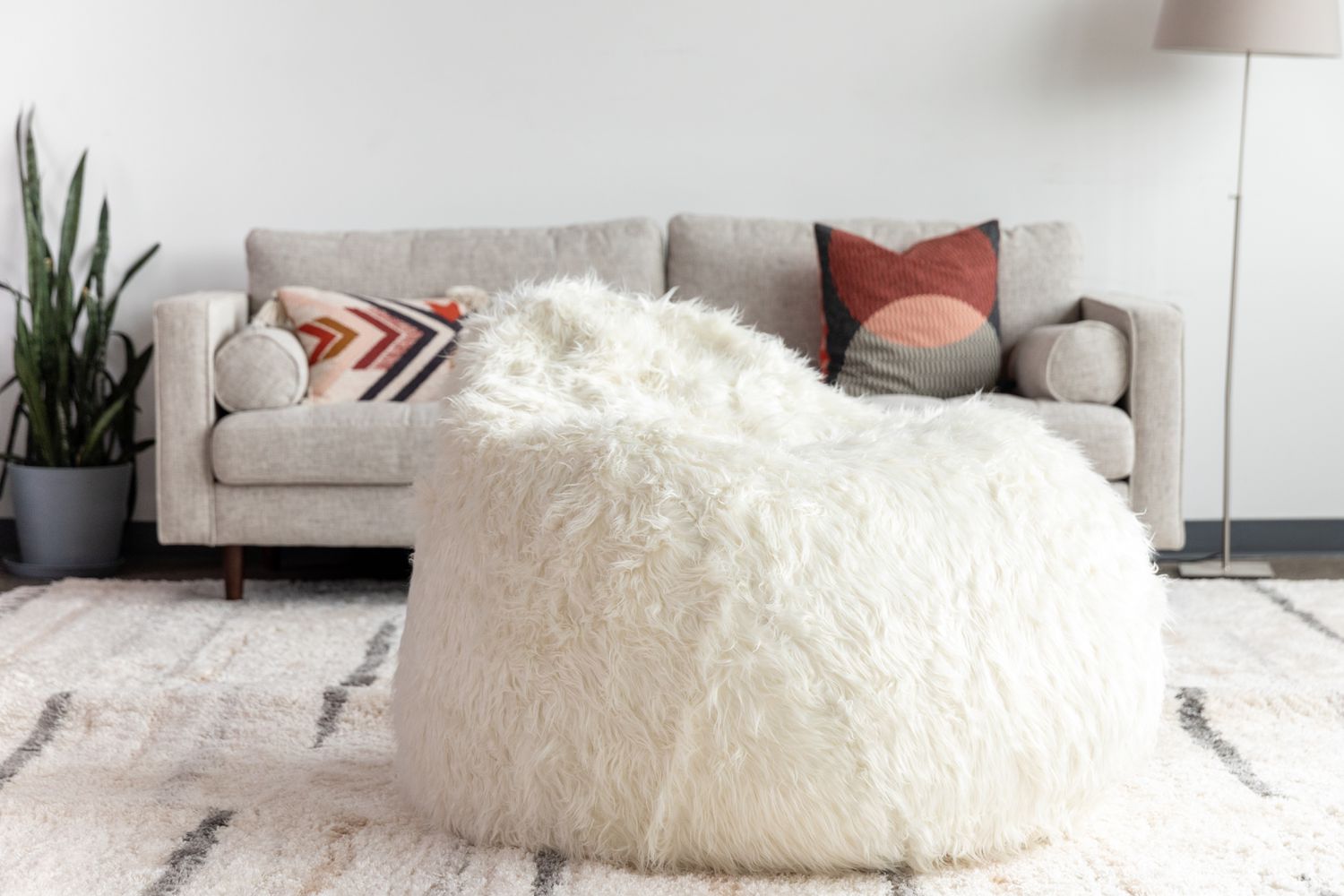 Aspyn Faux Fur Shag Bean Bag Chair displayed on carpet in front of couch